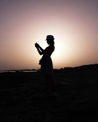 Side view of silhouette man standing on land against sunset sky