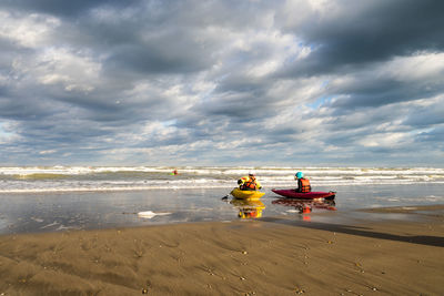 People sitting in kayak at beach against sky