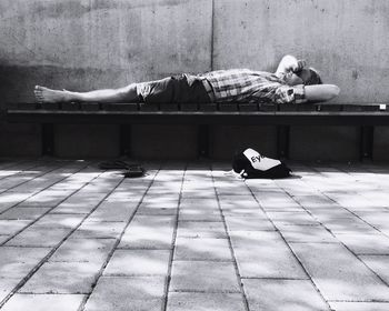 Side view of man sleeping on bench against wall