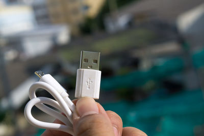 Close-up of hand holding usb cable against buildings