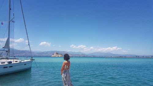 Side view of young woman standing by sea against blue sky