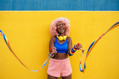 Portrait of young woman with arms crossed standing against yellow wall