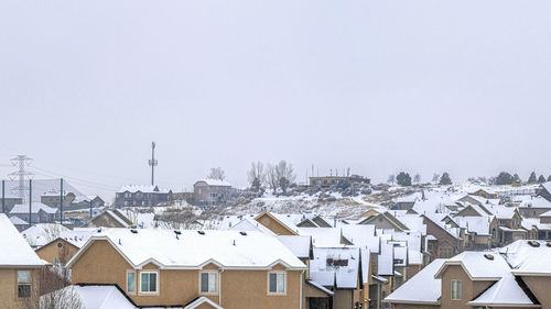 Houses by snow covered city against clear sky