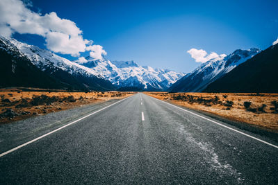 Empty road leading towards mountains against sky