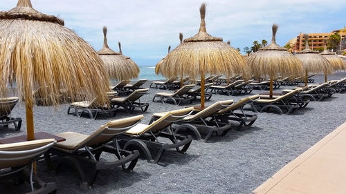 Deck chairs with parasols arranged at beach against cloudy sky