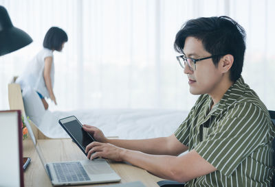 Side view of man using laptop and mobile phone on table at home