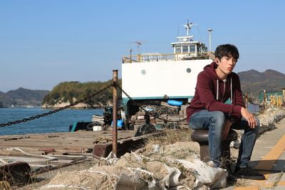 Young man sitting on boat against sky