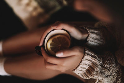 Female hands in knitted cozy sweater holding a mug of hot lemon tea. view from above. cozy winter 