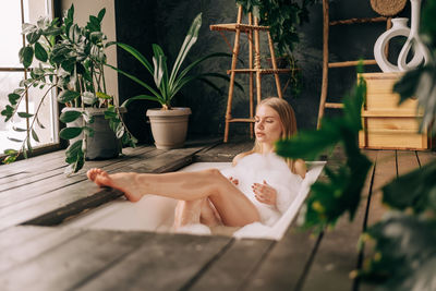 Woman taking bath with bubbles enjoing wellness and wellbeing in the room with natural houseplant