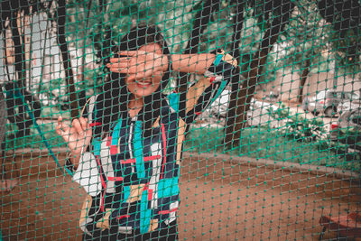 Young woman standing with mask by fence outdoors