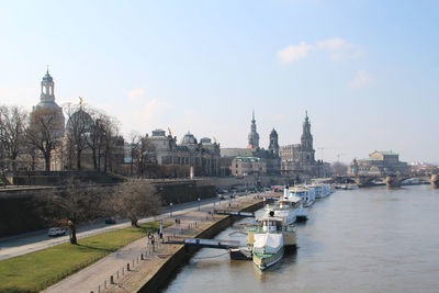 Ships moored in river in city against sky