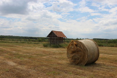 Hay bales on field against cloudy sky