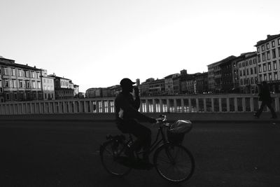 Man riding bicycle on bridge in city against clear sky