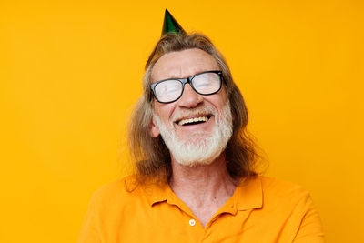 Portrait of smiling senior man wearing party hat against yellow background