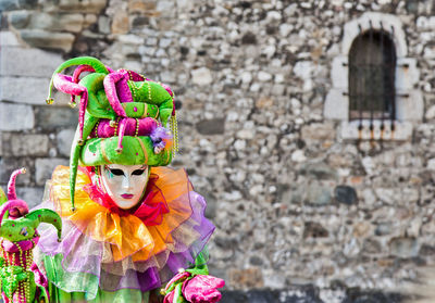 Person in costume and mask during carnival against wall in city