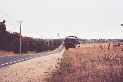 Road amidst field against clear sky