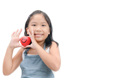 Portrait of smiling girl holding heart shape against white background