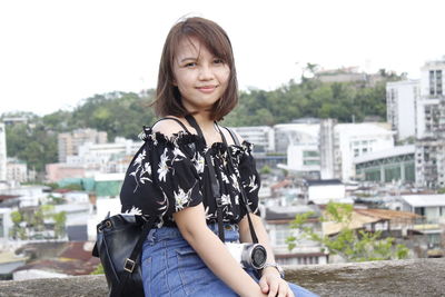 Portrait of beautiful young woman standing against city