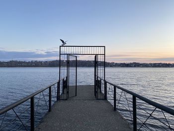 Pier over river against sky during sunset