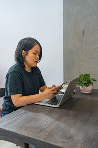 Young woman using phone while sitting on table