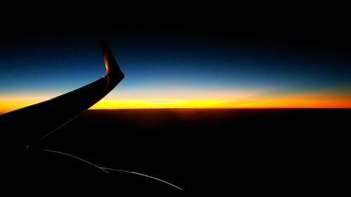 Silhouette airplane flying against sky during sunset