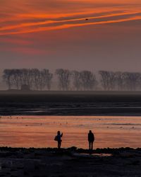 Silhouette people standing on landscape against orange sky