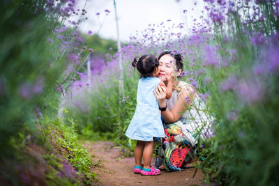 Girl kissing mother amidst flowers on field