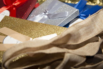 Gold, red, silver, and blue christmas boxes next to burlap ribbon