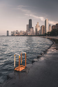 Sea by cityscape against sky during sunset