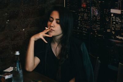 Young woman smoking cigarette while sitting at restaurant