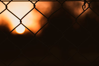 Close-up of chainlink fence against sky during sunset