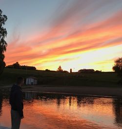 Silhouette man by river against orange sky