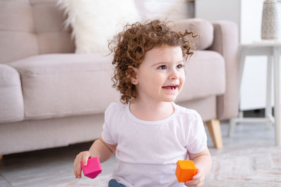 Portrait of cute girl playing with toy while sitting on sofa at home