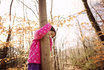 Portrait of girl embracing tree trunk at yard during autumn