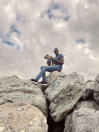Rear view of woman sitting on rock against sky