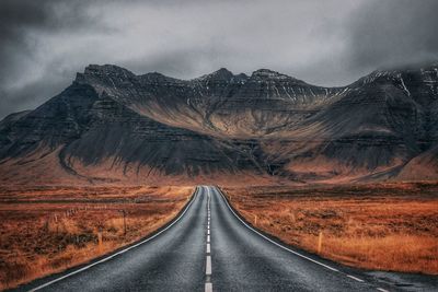 Road leading towards mountains against sky