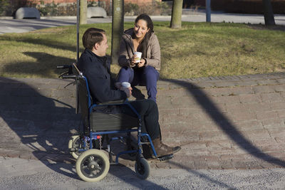 Young woman and man on wheelchair having coffee break