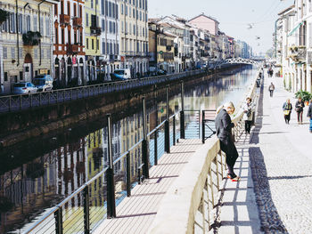 People on bridge over canal amidst buildings in city