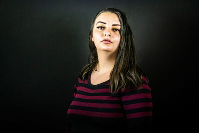 Portrait of young woman standing against black background