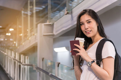 Portrait of woman drinking coffee while standing at airport