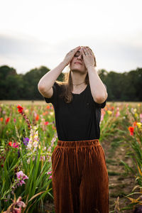 Woman with hands covering eyes standing amidst flowers