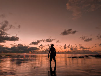 Silhouette man standing on shore against sky during sunset