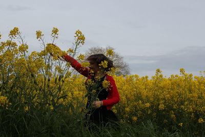 Young woman amidst yellow flowers against sky