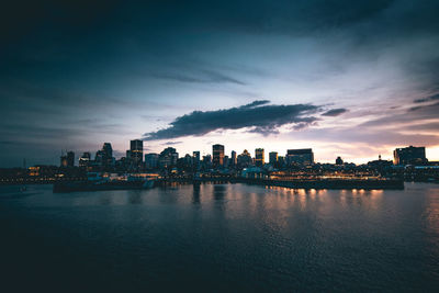 Scenic view of river by buildings against sky at dusk