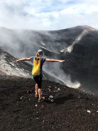 Rear view of woman standing with arms outstretched at volcanic crater
