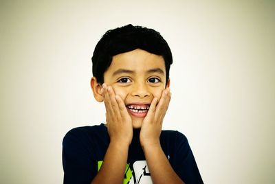 Portrait of smiling boy with hands on chin against white background