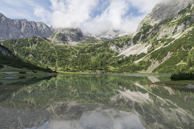 Scenic view of lake and rocky mountains against cloudy sky