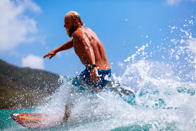 Shirtless man surfing on sea against sky