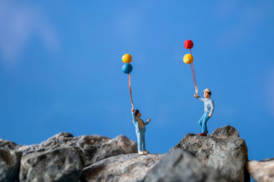 Low angle view of people on rocks against blue sky