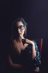 Young woman wearing eyeglasses sitting against black background